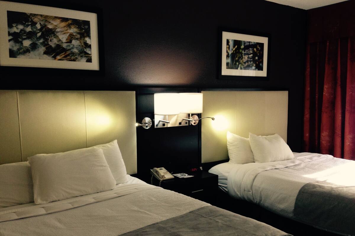 A hotel room with two beds, a nightstand with a lamp, and artwork on the walls.