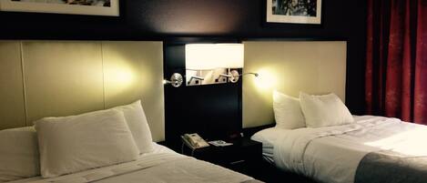 Ett hotellrum med två sängar, ett nattduksbord med en lampa och konstverk på väggarna.