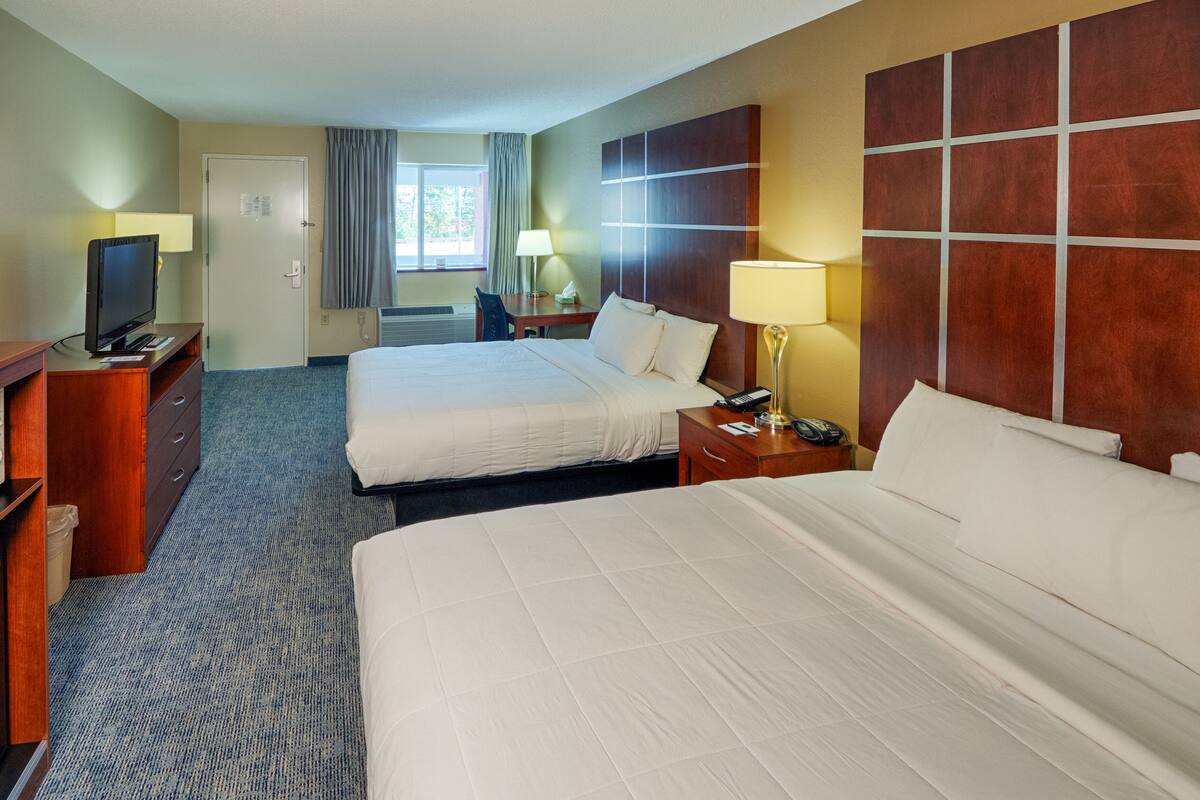A hotel room with two beds, a desk with a TV, a lamp, and a window with curtains.