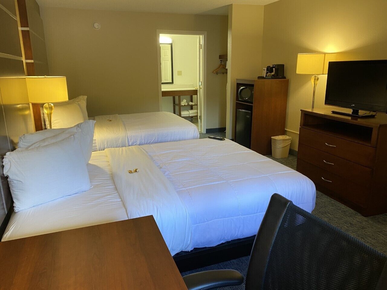 Habitación de hotel con dos camas, un escritorio, una silla, un televisor y un baño pequeño.