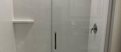 Un box de ducha con paredes de vidrio, un cabezal de ducha de mano, una puerta de vidrio y suelo de baldosas blancas.