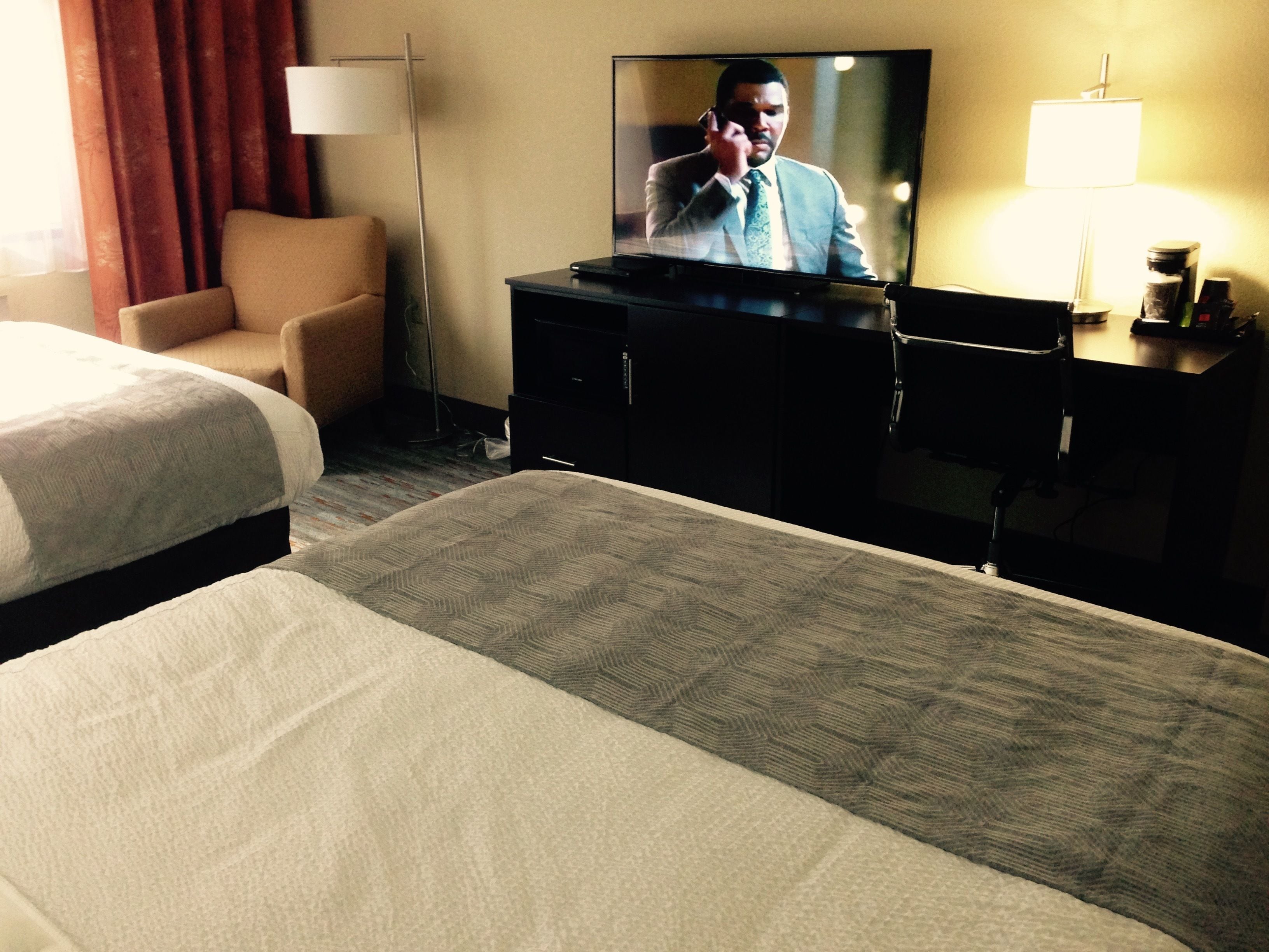 Una habitación de hotel con cama, televisión sobre un mueble bajo, escritorio y silla.