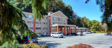 A multi-story hotel with a parking lot, surrounded by trees and shrubs.