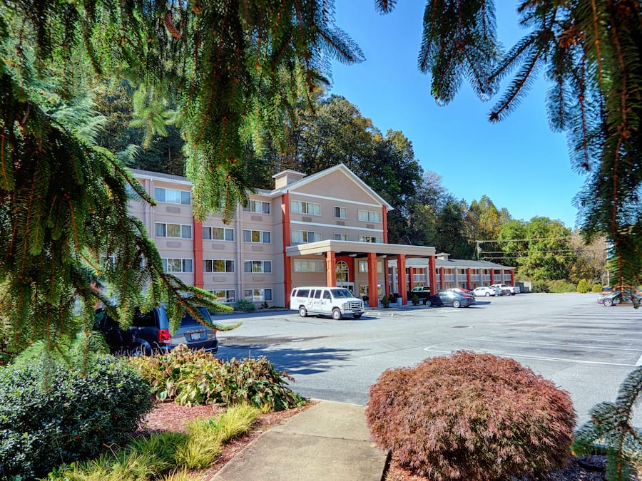 A multi-story hotel with a parking lot, surrounded by trees and shrubs.