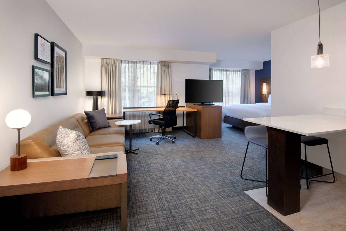 Une chambre d’hôtel avec un canapé, un bureau et une chaise, une télévision, un lit et une petite table.
