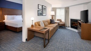 A hotel room with a bed, a sofa, a TV, a fireplace, and framed pictures on the wall. - Sonesta ES Suites Atlanta Alpharetta North Point Mall (Alpharetta)