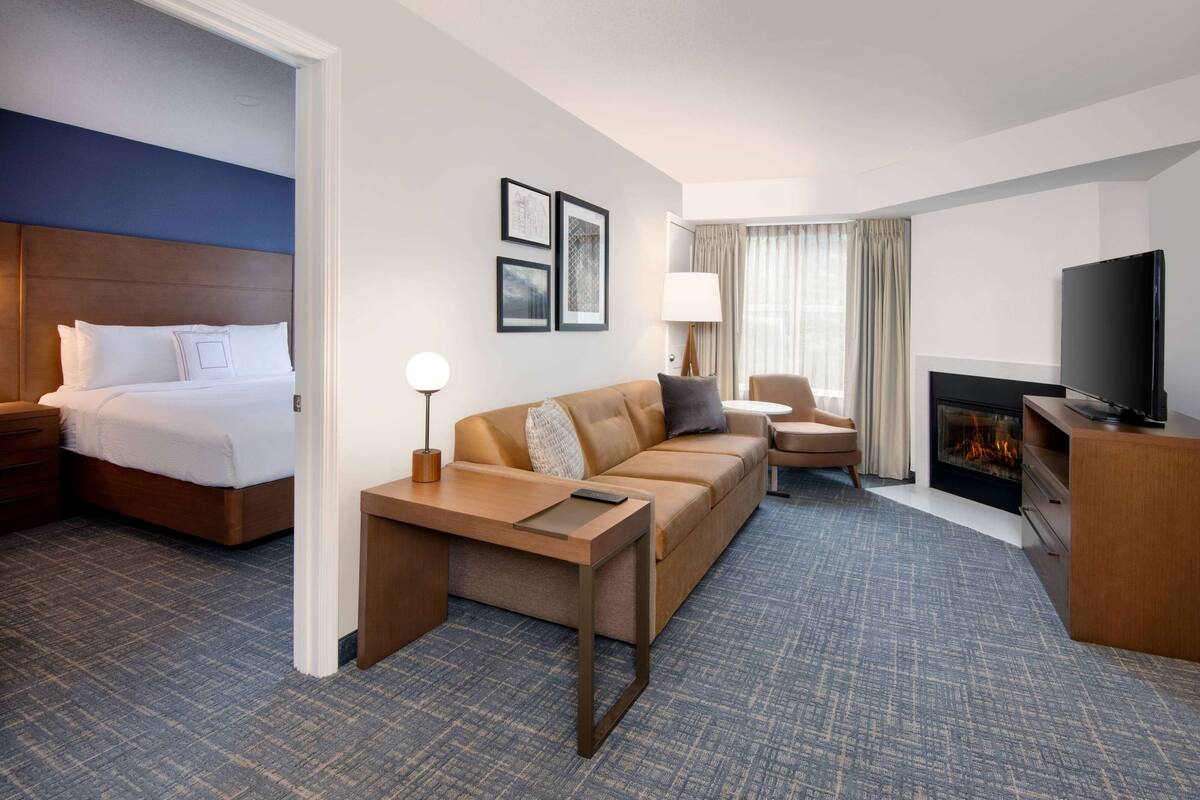 Une chambre d’hôtel avec un lit, un canapé, une télévision, une cheminée et des tableaux encadrés au mur.