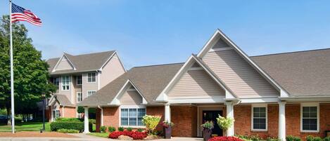A row of brick townhouses with pitched roofs, a flagpole with an American flag, and well-maintained landscaping.