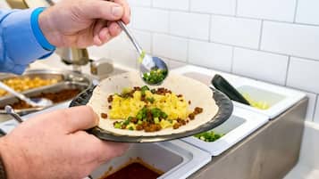 A person holding a plate with a food item topped with green onions.
