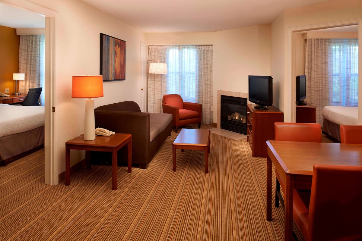 Ein Hotelzimmer mit Bett, Sofa, einem kleinen Tisch, Fernseher, Kamin und einem Fenster mit Vorhängen.