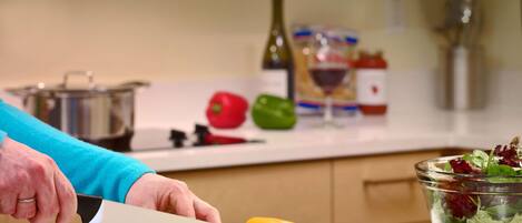 A kitchen with a person slicing a yellow bell pepper on a cutting board, a bowl of salad, and various kitchen items in the background.