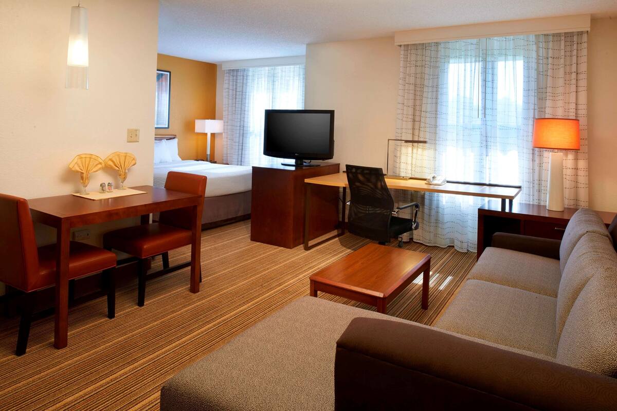 Ein Hotelzimmer mit Bett, Fernseher, Schreibtisch mit Stuhl, Sofa und kleinem Tisch.