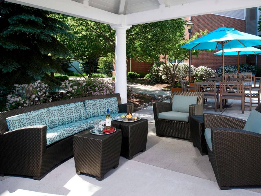 An outdoor patio area with wicker furniture, including a sofa and chairs, and a table with a tray of food and drinks.