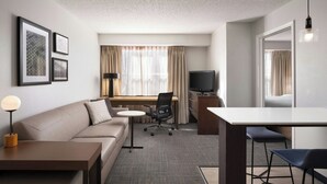 Une chambre d’hôtel moderne, équipée d’un canapé, d’un bureau, d’une chaise, d’une télévision et de tableaux encadrés au mur.