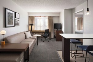 Una habitación de hotel moderna con un sofá, un escritorio, una silla, un televisor y cuadros en la pared.