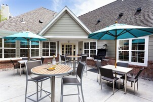 Un patio con mobiliario exterior, una parrilla y sombrillas.