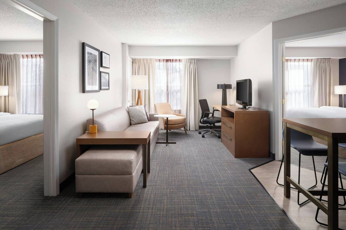 A hotel room with a bed, a sofa, a desk, a chair, and a TV.