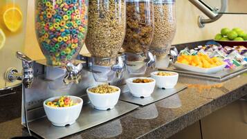 Un buffet proposant des distributeurs de céréales et de granola, des bols de céréales et un plateau de fruits.