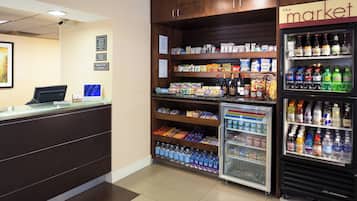 Una zona de recepción con mostrador, un refrigerador lleno de bebidas y estantes con aperitivos y agua embotellada.