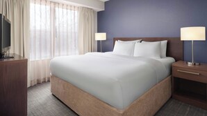 Une chambre d’hôtel avec un grand lit, deux tables de chevet, une télévision et une fenêtre avec des rideaux.