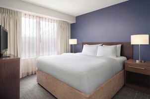 Una habitación de hotel con una cama grande, dos mesitas de noche, un televisor y una ventana con cortinas.
