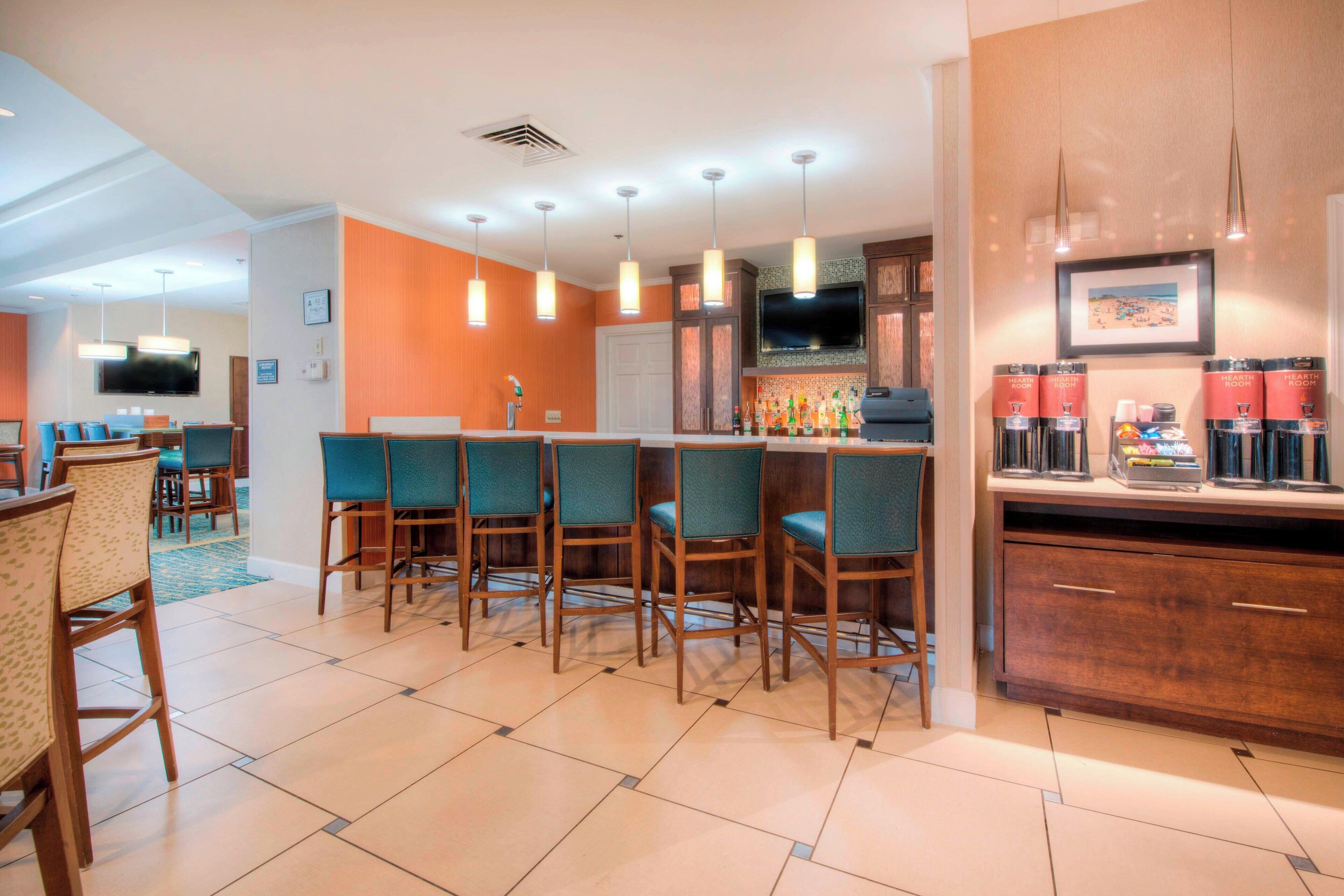 A modern kitchen with a bar area, featuring wooden cabinets, a tiled floor, and pendant lighting.