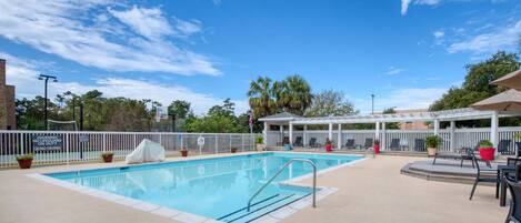 A swimming pool with a white fence, lounge chairs, and a covered seating area.