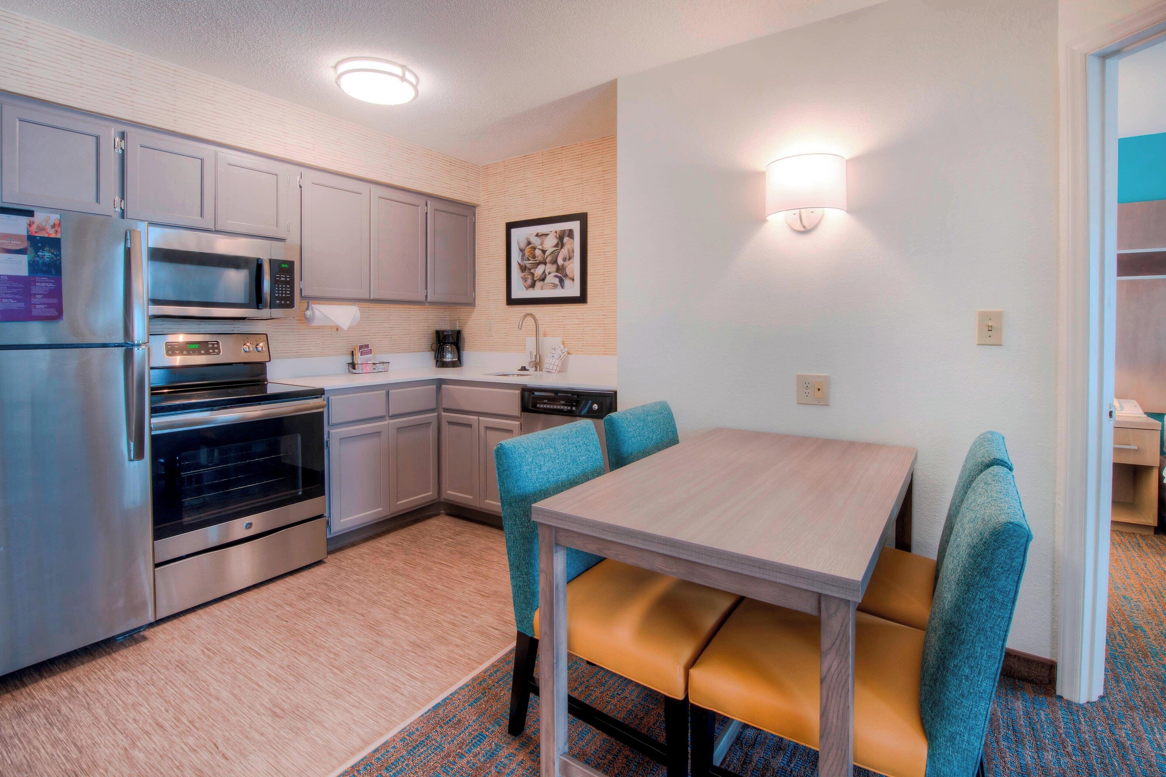 A compact kitchen with a refrigerator, microwave, oven, and sink. There is a dining table with two chairs and a light fixture above it.