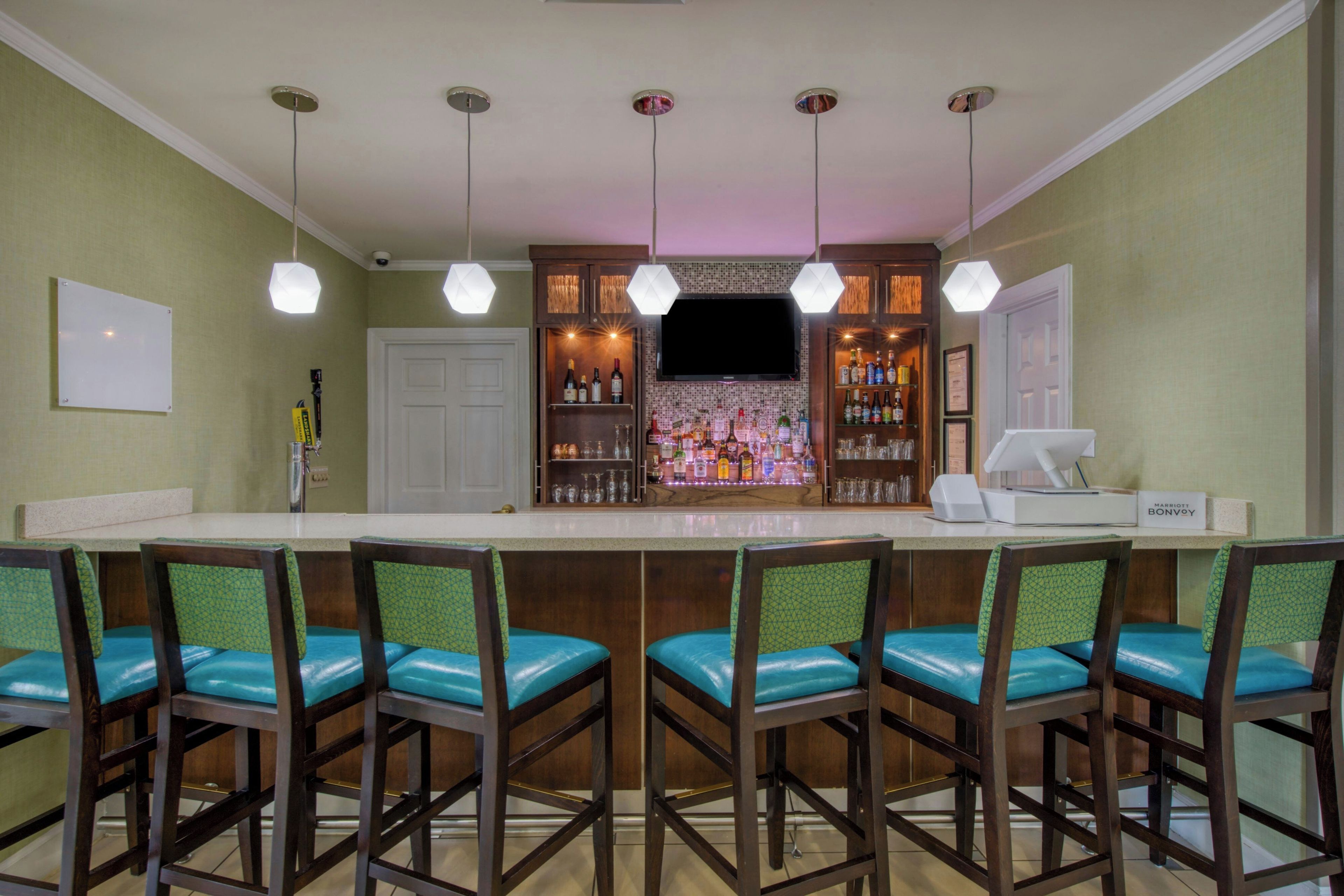 A bar area with a counter, multiple bar stools, and a television screen above the bar.