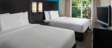 A hotel room with two beds, a TV, and a window with a view of trees.