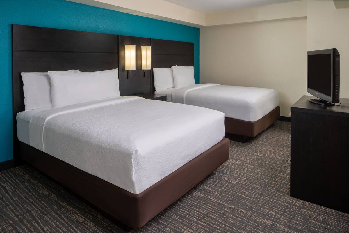 A hotel room with two beds, a TV, and a desk.