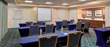 A conference room with tables and chairs, a projector screen, and a water dispenser.
