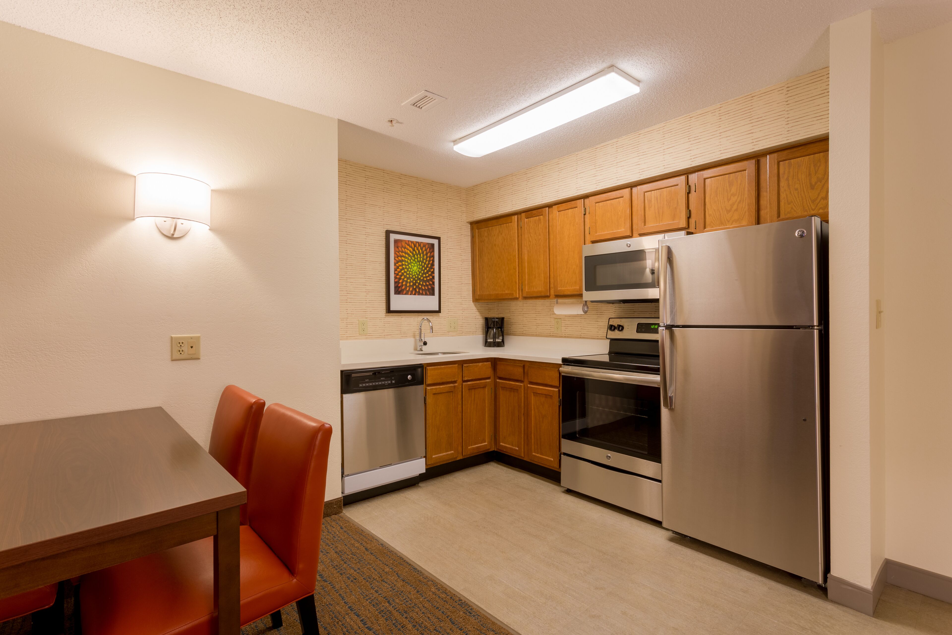 A compact kitchen with wooden cabinets, a stainless steel refrigerator, an oven, and a dishwasher.