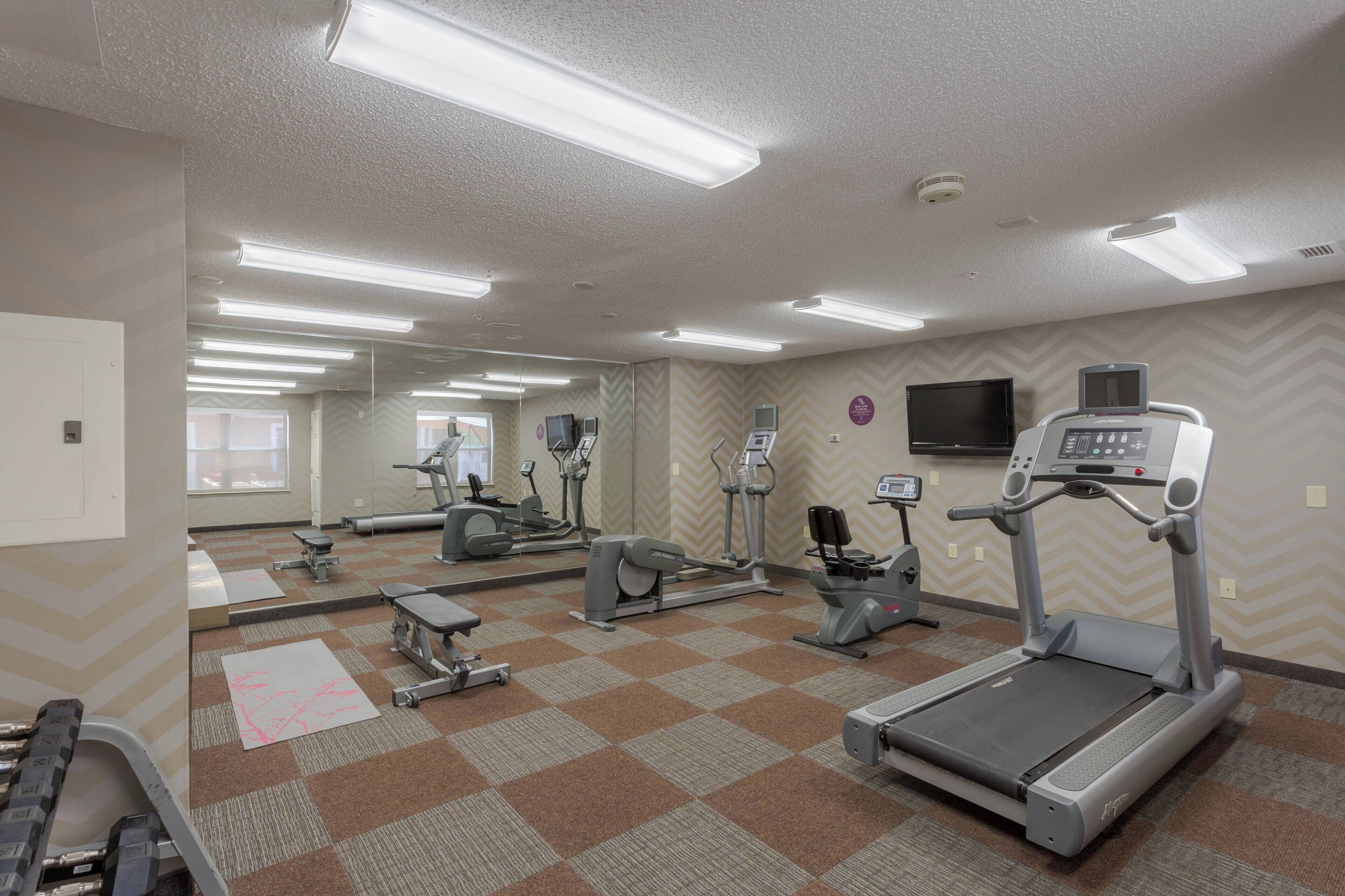 Une salle de sport équipée de divers appareils d’exercice, notamment des tapis de course, des vélos d’appartement et des appareils de musculation.