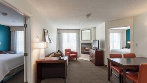 A hotel room with a bed, desk, chairs, a TV, and a fireplace. - Residence Inn by Marriott Rocky Mount (Rocky Mount)