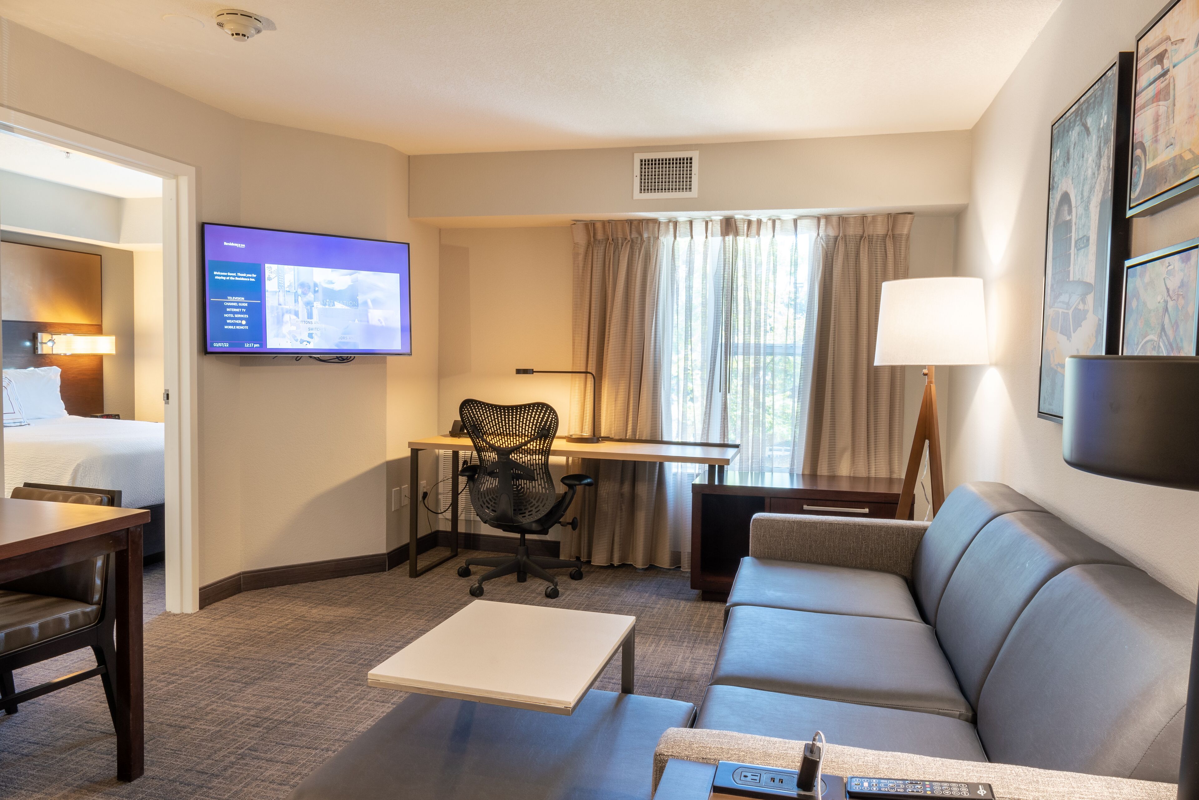 A hotel room with a bed, a desk, a computer, a TV, a sofa, and a coffee table.