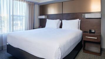 A large bed with white linens, a wooden headboard, a bedside table with a phone, and a window with curtains.