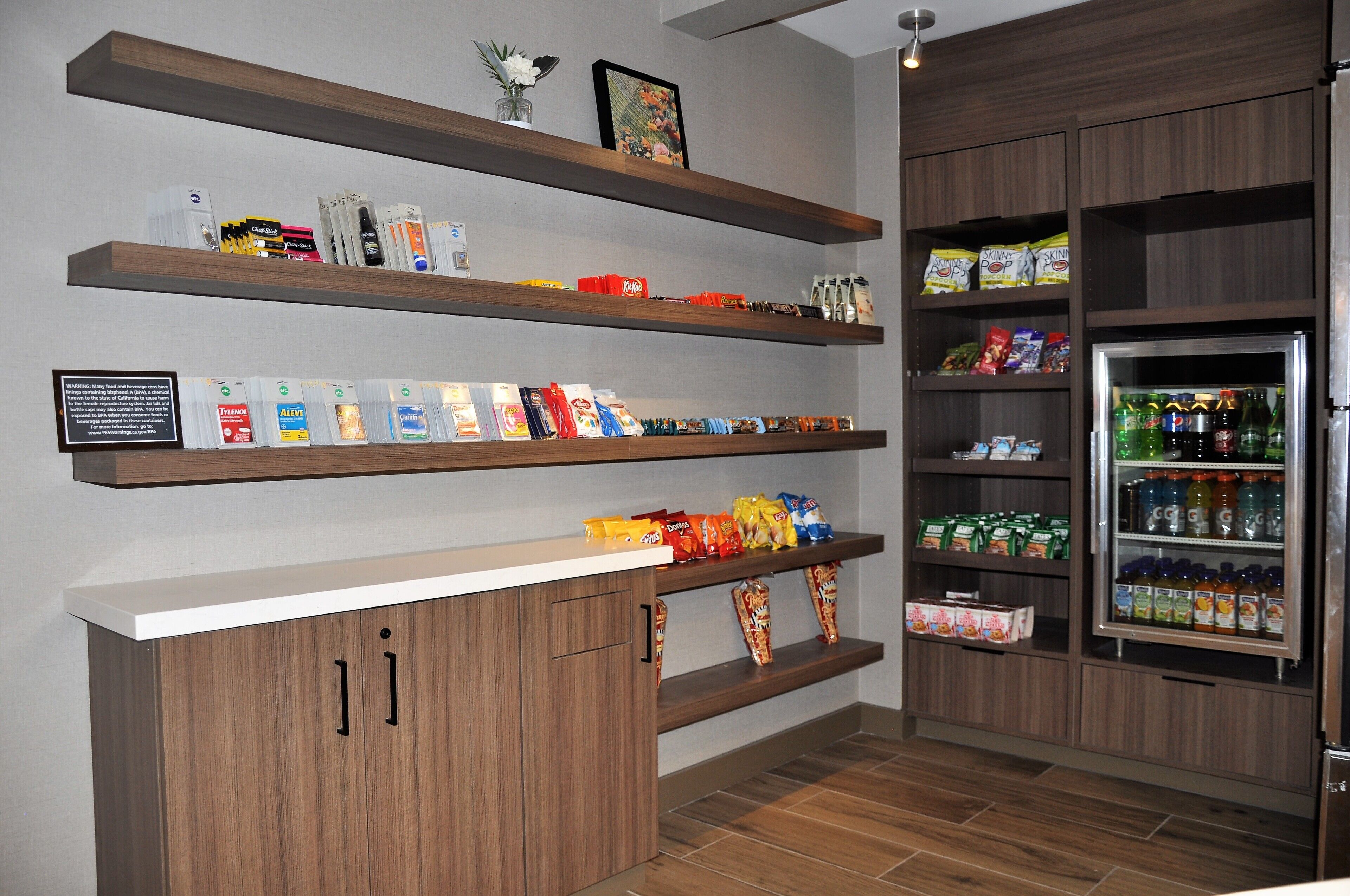 A snack bar with shelves stocked with various snacks and beverages, a refrigerator with drinks, and a small display area with a framed picture.