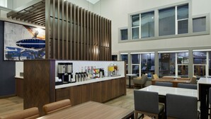 Un hall d’hôtel moderne doté d’un bar central, de différents espaces aménagés pour s’asseoir et de grandes fenêtres laissant entrer la lumière naturelle.