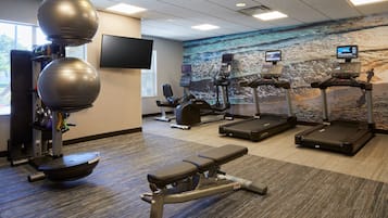 A gym with exercise equipment, a bench, treadmills, and a wall-mounted TV.