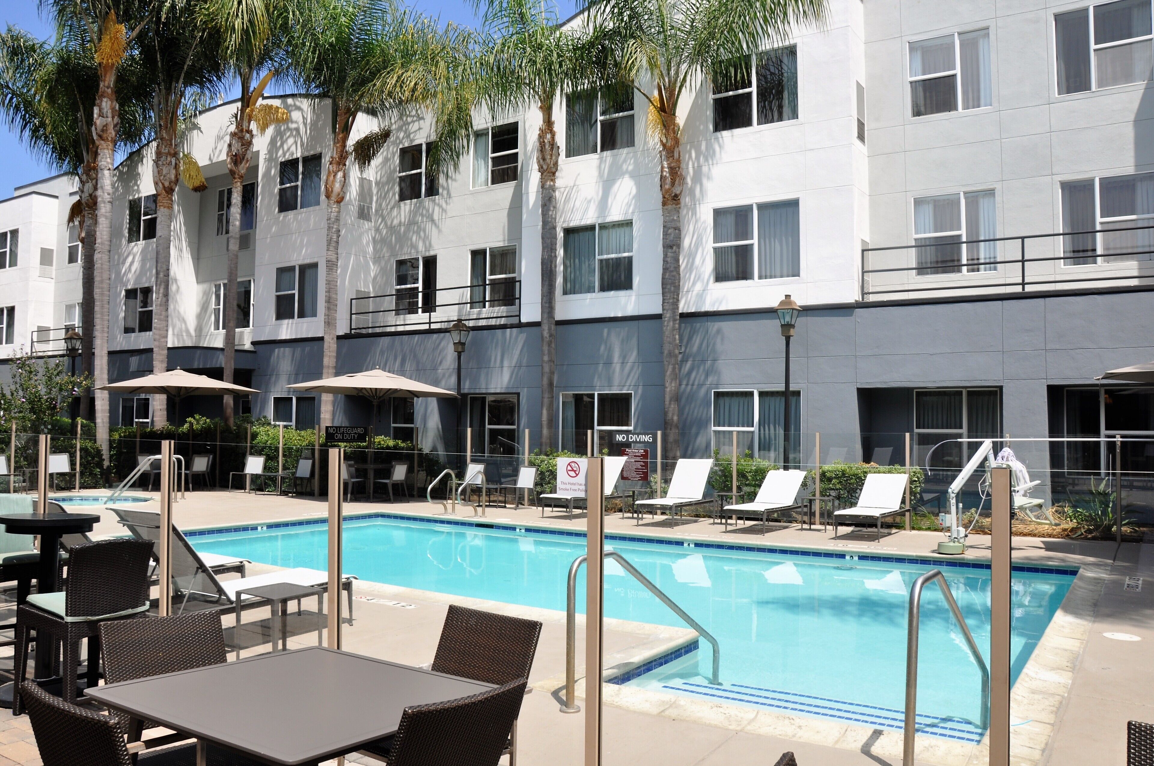 A hotel pool area with lounge chairs, a table, and a sign indicating no lifeguard on duty.