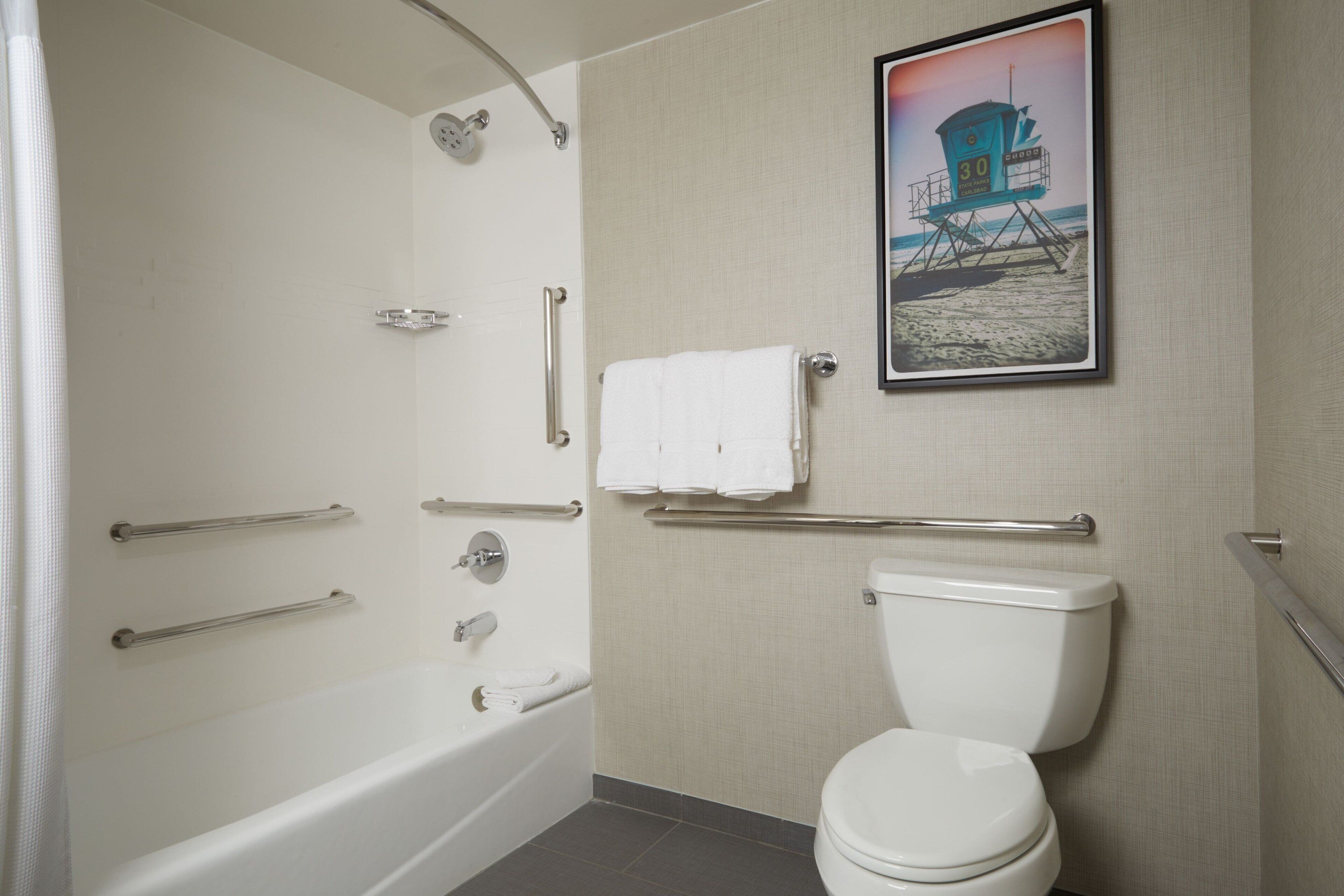 A bathroom with a bathtub, toilet, and a framed picture of a lifeguard tower on the wall.