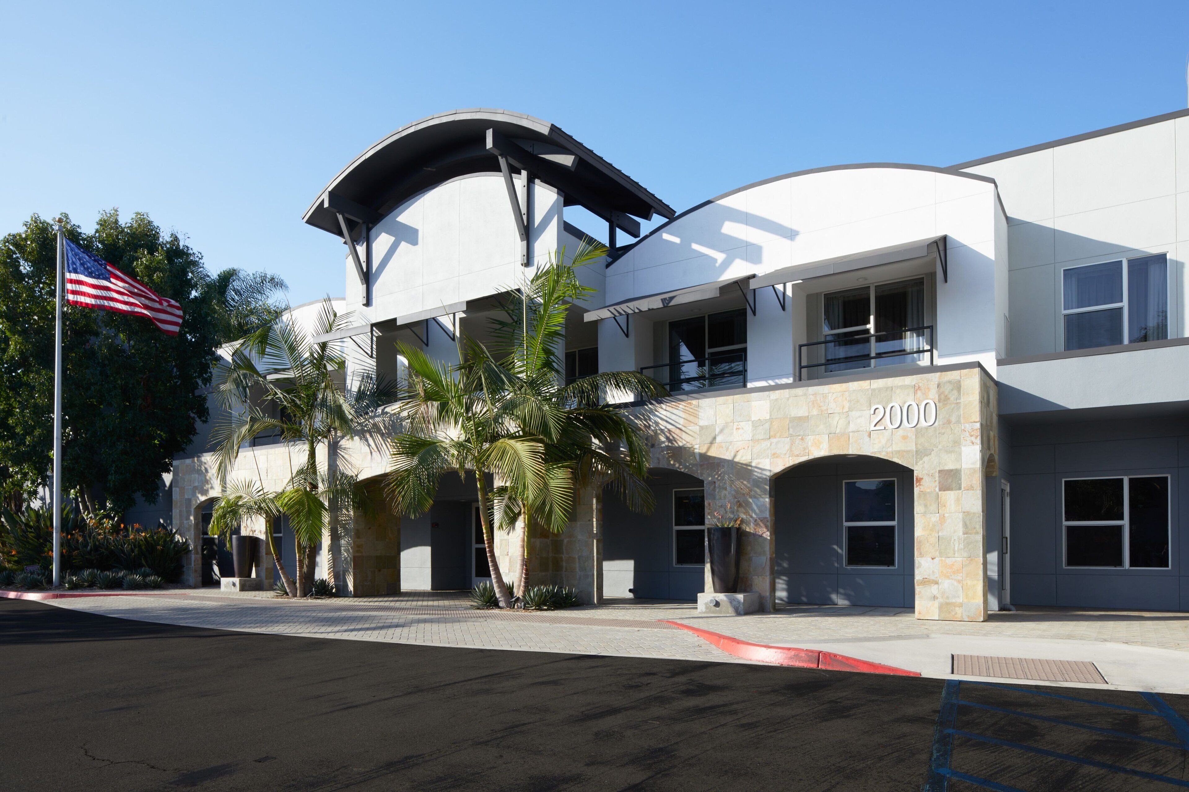 A modern building with a curved roof, a flag, and palm trees.