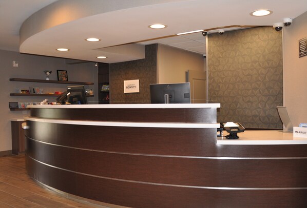 A reception desk with a dark wood finish, a computer monitor, and a sign indicating the name of the hotel.