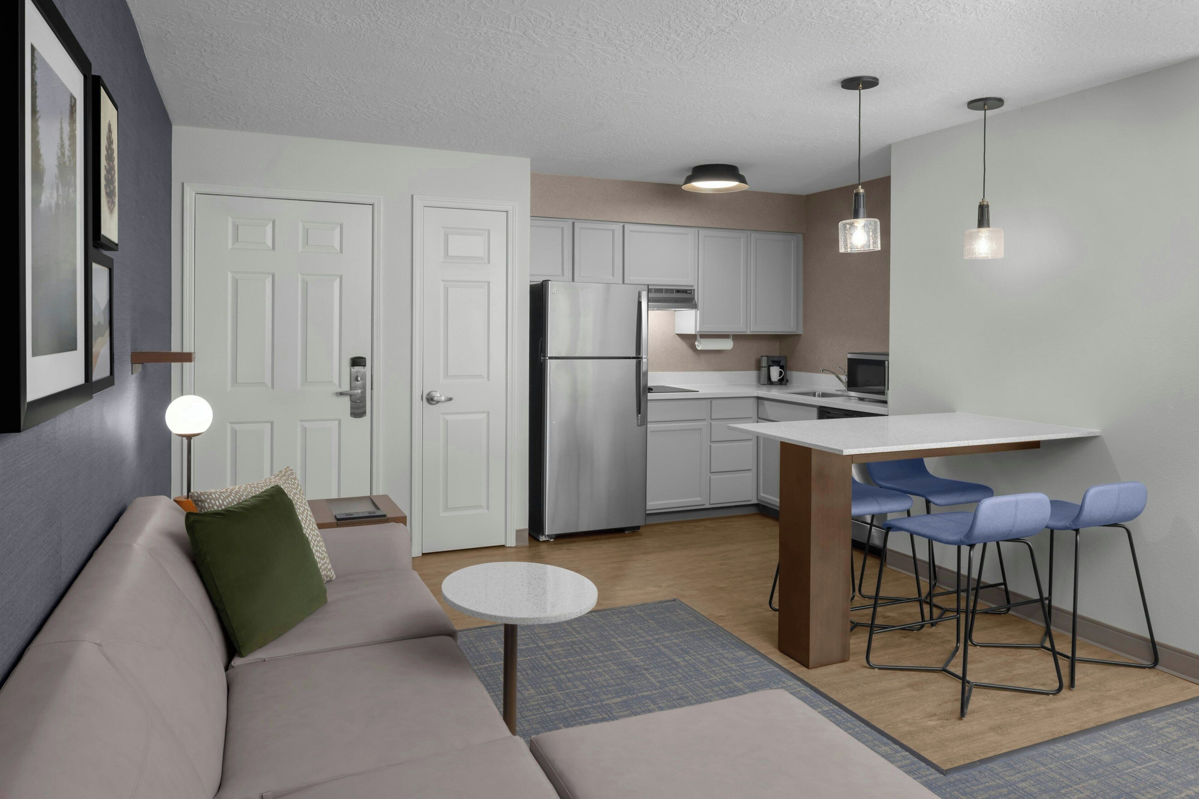 A modern kitchen with white cabinets, a stainless steel refrigerator, and a bar area with blue bar stools.