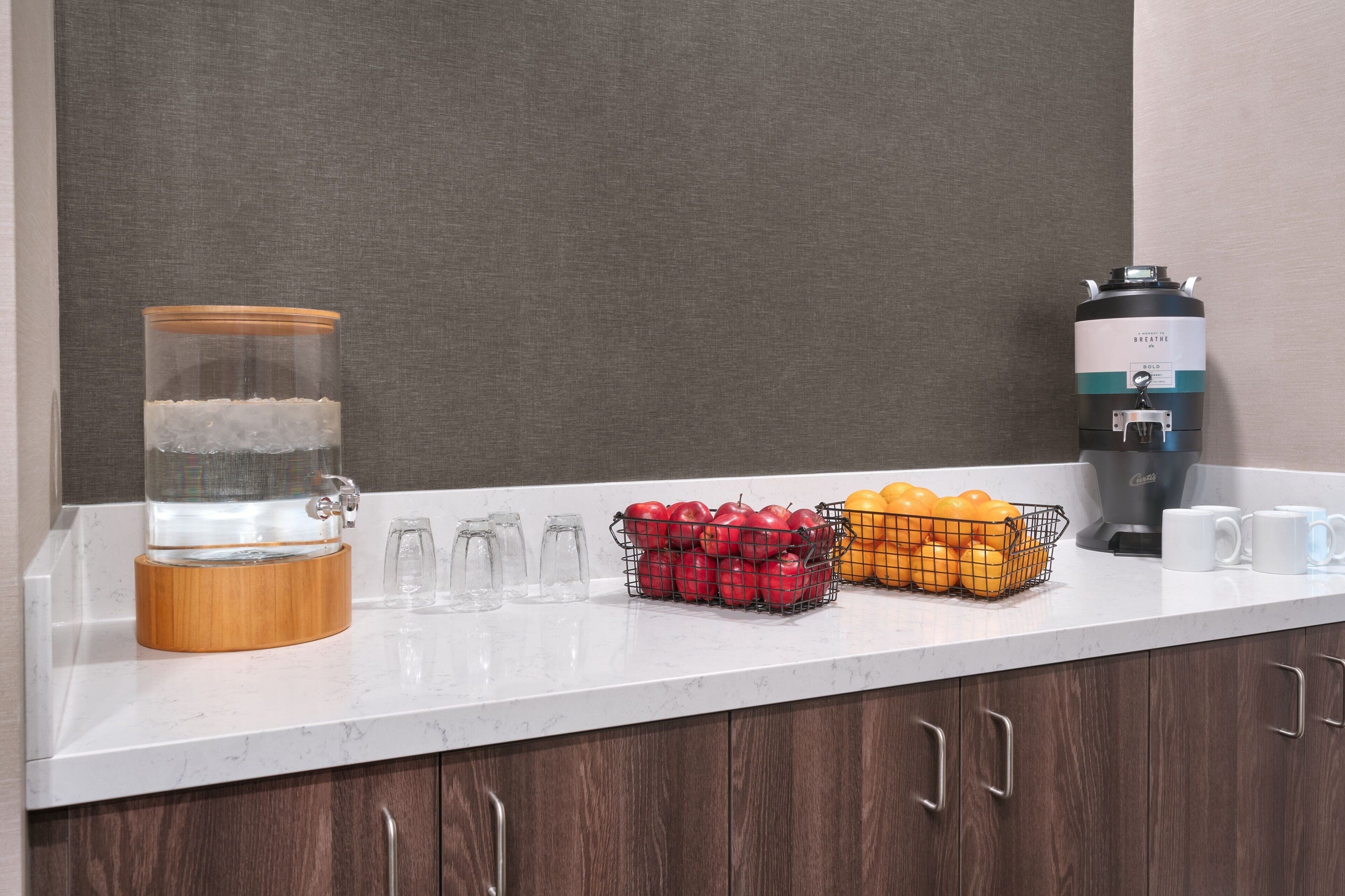 A kitchen counter with a water dispenser, a coffee maker, and fruit baskets.
