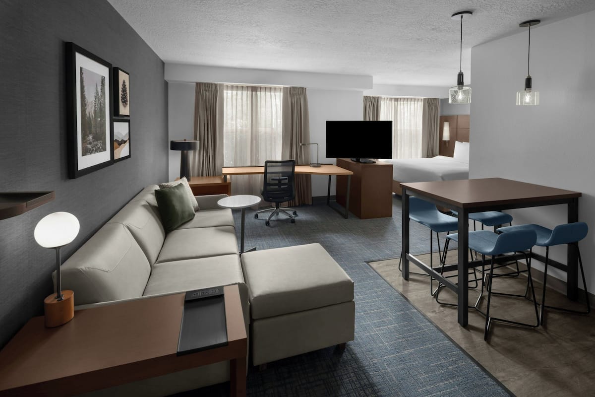 Une chambre d’hôtel moderne équipée d’un canapé, d’un bureau, d’une télévision et d’un coin repas.
