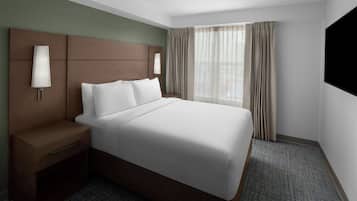 A hotel room with a large bed, a nightstand, a lamp, a TV, and a window with curtains.