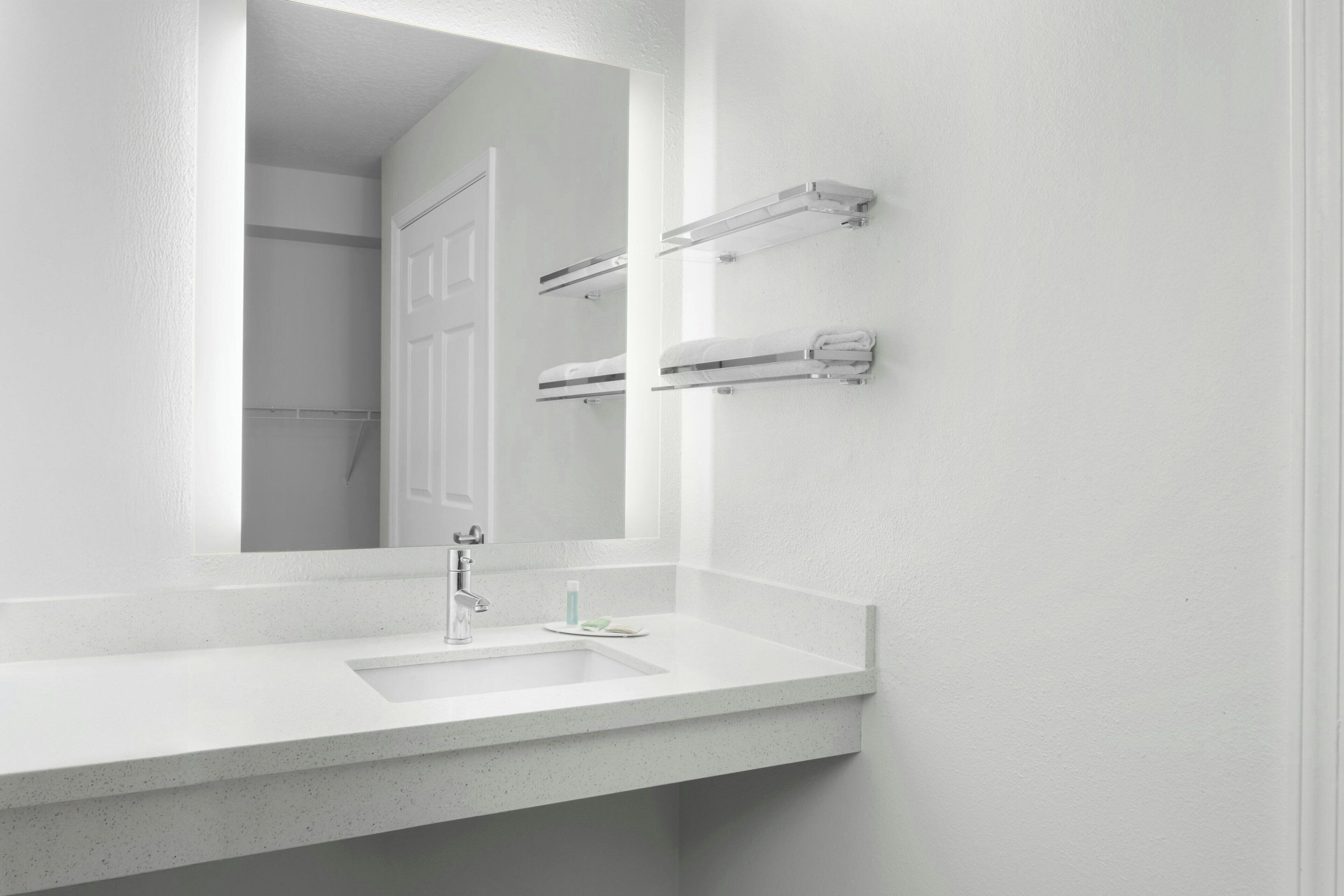A bathroom with a white sink, a mirror, and towel racks on the wall.