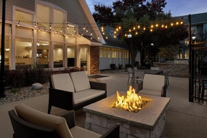 Un área de patio al aire libre con un hogar a leña de piedra, mobiliario de mimbre e iluminación con luces colgantes.